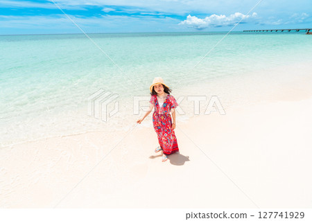 A young woman in a dress walking along the water's edge on a tropical beach A young woman in a dress walking along the water's edge on a tropical beach 127741929