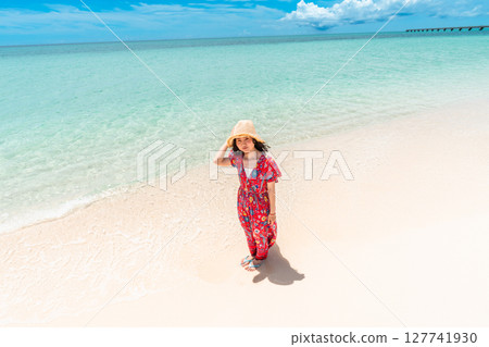 A young woman in a dress walking along the water's edge on a tropical beach 127741930
