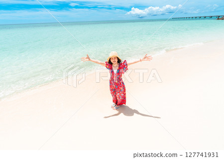 A young woman in a dress walking along the water's edge on a tropical beach 127741931