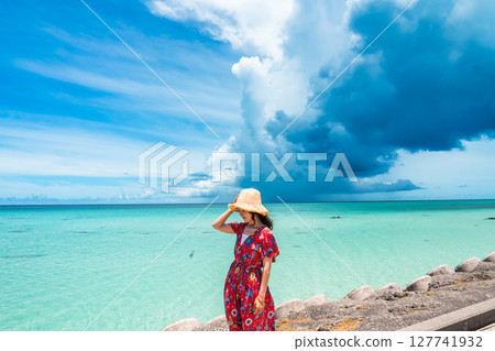 一位身穿洋裝的年輕女子在熱帶海灘的水邊散步 127741932