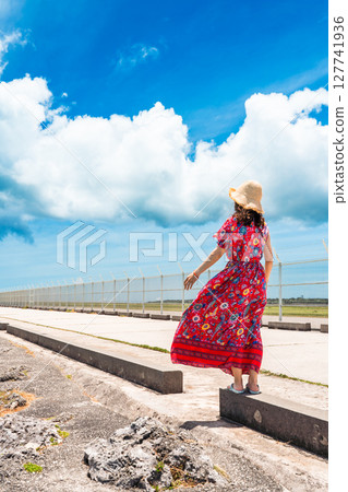 A young woman in a dress walking along the water's edge on a tropical beach 127741936