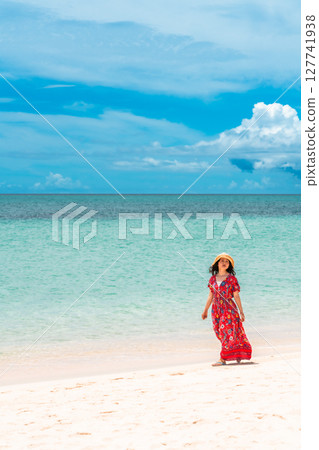 A young woman in a dress walking along the water's edge on a tropical beach 127741938