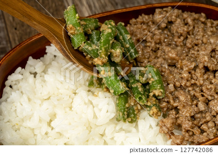 準備一份三餐的蓋飯午餐。把肉末、芝麻醬四季豆和炒蛋放在飯上。 127742086