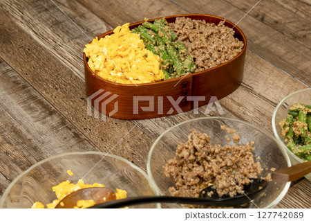 Pack a three-meal rice bowl lunch. Place minced meat, green beans with sesame sauce, and scrambled eggs on rice. Pack a three-meal rice bowl lunch. Place minced meat, green beans with sesame sauce, and scrambled eggs on rice. 127742089
