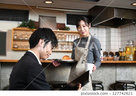 A female waiter serving food to a male customer at a restaurant 127742621