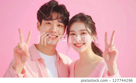 一對夫婦在粉紅色背景上做出和平手勢 一對夫婦在粉紅色背景上做出和平手勢 127744296