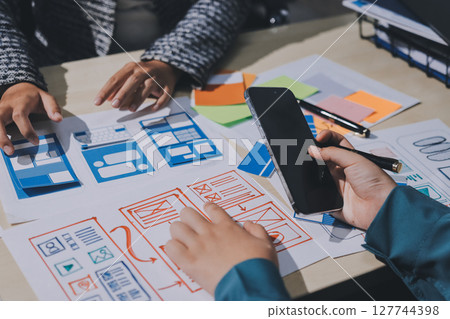 Group of young application developers analyzing uxui mobile app templates during a working meeting Group of young application developers analyzing uxui mobile app templates during a working meeting 127744398