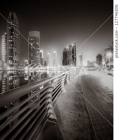 Urban city skyline with illuminated skyscrapers and waterfront railing in black and white at night, Dubai Marina bay UAE 127746806