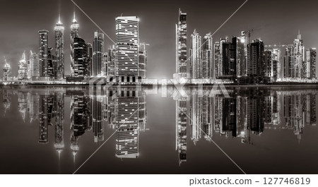 Urban city skyline with illuminated skyscrapers and waterfront railing in black and white at night, Dubai Marina bay UAE 127746819