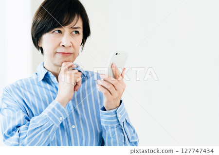 A middle-aged woman who operates a smartphone 127747434