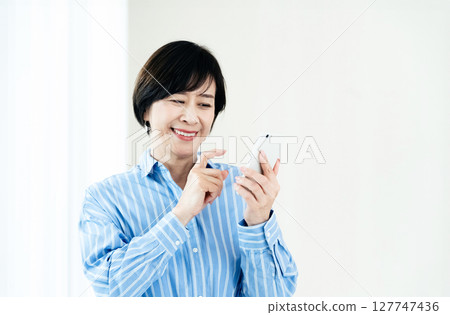 A middle-aged woman who operates a smartphone 127747436