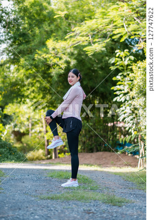 Woman in athletic wear stretching in a park, surrounded by greenery, ready for outdoor exercise. 127747622