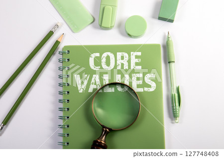 Core Values Text on Green Notebook with Magnifying Glass and Office Supplies on White Background 127748408