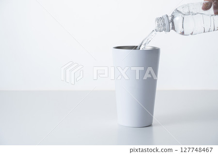 將瓶裝水倒入不銹鋼杯中 將瓶裝水倒入不銹鋼杯中 127748467