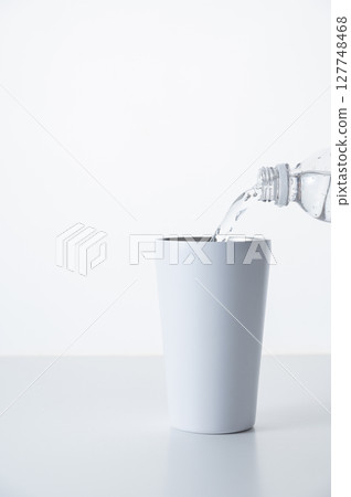 將瓶裝水倒入不銹鋼杯中 將瓶裝水倒入不銹鋼杯中 127748468