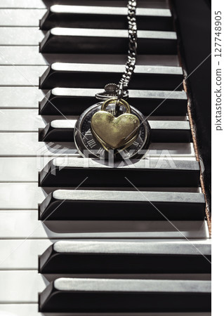Antique pocket watch (A retro pocket watch) with Golden heart shaped love padlock on Piano keys background. 127748905