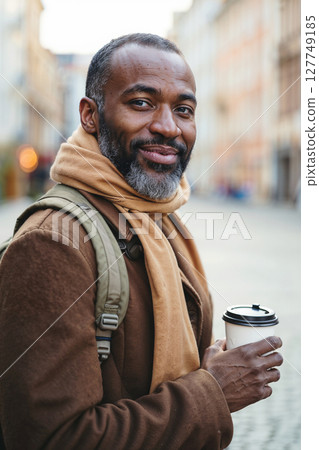 A close-up, eye-level shot captures a man smiling directly at the camera, holding a disposable hot beverage cup. A close-up, eye-level shot captures a man smiling directly at the camera, holding a disposable hot beverage cup. 127749185