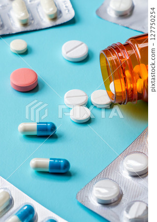 Close-up, high-resolution image of various pharmaceutical tablets and capsules of different shapes, sizes and colours neatly arranged on a clean white or light blue background. 127750254