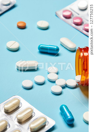 Close-up, high-resolution image of various pharmaceutical tablets and capsules of different shapes, sizes and colours neatly arranged on a clean white or light blue background. 127750255