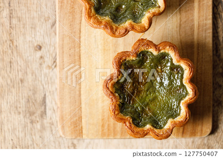 Closeup of Matcha and mochi Portuguese sweet dessert egg tart or Pastel de Nata on wooden board on wooden table. 127750407