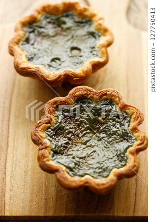 Closeup of Matcha and mochi Portuguese sweet dessert egg tart or Pastel de Nata on wooden board on wooden table. 127750413