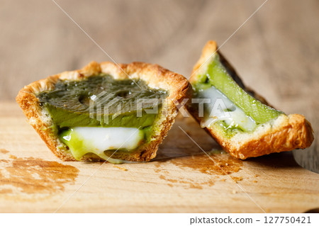 Closeup of Matcha and mochi Portuguese sweet dessert egg tart or Pastel de Nata on wooden board on wooden table. 127750421