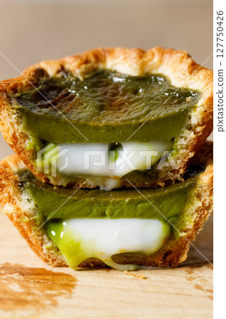 Closeup of Matcha and mochi Portuguese sweet dessert egg tart or Pastel de Nata on wooden board on wooden table. 127750426