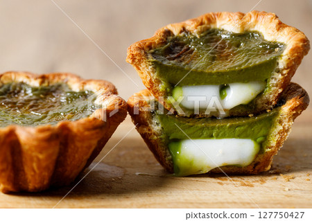 Closeup of Matcha and mochi Portuguese sweet dessert egg tart or Pastel de Nata on wooden board on wooden table. 127750427