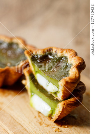 Closeup of Matcha and mochi Portuguese sweet dessert egg tart or Pastel de Nata on wooden board on wooden table. Closeup of Matcha and mochi Portuguese sweet dessert egg tart or Pastel de Nata on wooden board on wooden table. 127750428