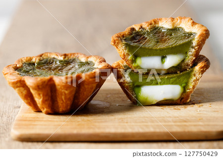 Closeup of Matcha and mochi Portuguese sweet dessert egg tart or Pastel de Nata on wooden board on wooden table. 127750429