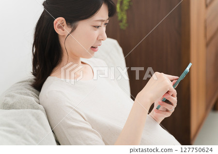 Pregnant woman operating a smartphone on the sofa Lifestyle image 127750624