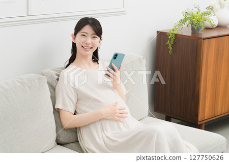 孕婦在沙發上操作智慧型手機的生活風格影像 孕婦在沙發上操作智慧型手機的生活風格影像 127750626