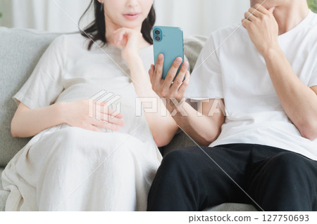 Pregnant woman and husband operating a smartphone Lifestyle image 127750693