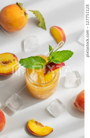 Refreshing peach cocktail, lemonade or iced tea on a white table with shadows, ice cubes and fruits. 127751128