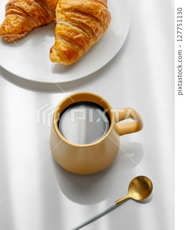 Coffee espresso in yellow cup and fresh croissants on a white background with morning shadows 127751130