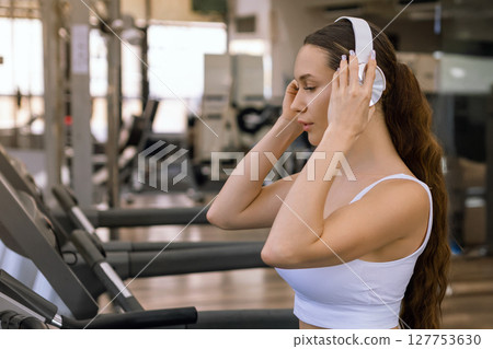 Young sporty woman running on machine in the gym and listening music in headphones 127753630