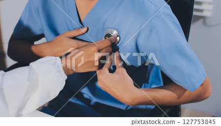 A physician uses a stethoscope to examine a patient's heart during a clinic appointment. 127753845