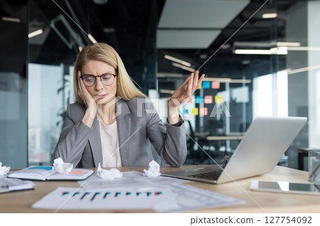 Disappointed and upset woman at workplace, businesswoman financier dissatisfied with bills and financial report, sitting unhappy with paperwork inside office with laptop. 127754092