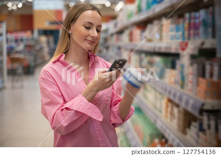 Woman choosing medicine in pharmacy scanning products with smartphone 127754136