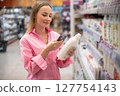 Woman using smartphone scanning products in supermarket 127754143