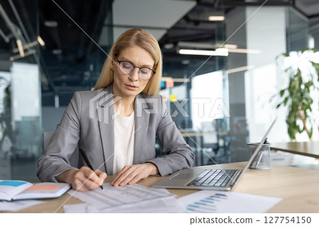 Serious focused woman doing paperwork inside office. Businesswoman financier accountant preparing financial report and filling out tax forms. Office worker with documents thinking. 127754150