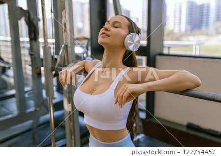Sexy girl wearing sportswear is posing next smith machine in the fitness center. Sexy girl wearing sportswear is posing next smith machine in the fitness center. 127754452