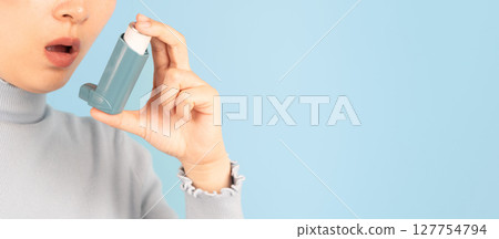 Young female using blue asthma inhaler for relief asthma attack. Pharmaceutical products is used to prevent and treat wheezing and shortness of breath caused asthma or COPD. Close up. 127754794