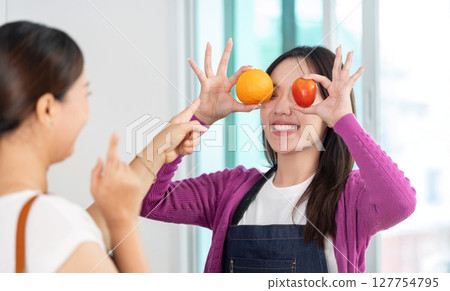 Healthy Lifestyle and Fun Cooking. Two women enjoying playful moments with fruits in a bright kitchen. Healthy Lifestyle and Fun Cooking. Two women enjoying playful moments with fruits in a bright kitchen. 127754795
