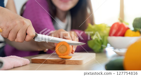 Chopping Fresh Vegetables. Close-up of a woman slicing a carrot while another woman observes. 127754816