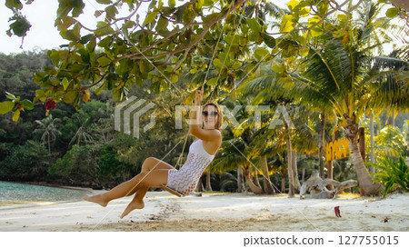 Pretty woman spends her vacation at the seaside. Sexy hot daring girl is swinging on a swing. Concept natural beauty body health, sensuality, lifestyle alone travel, relaxation. 127755015