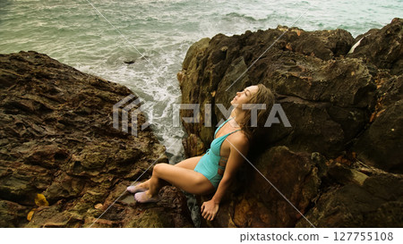 Woman meditates, relaxes on rock crack reef hill in stormy morning cloudy sea. Mother of ocean gives birth to him Woman meditates, relaxes on rock crack reef hill in stormy morning cloudy sea. Mother of ocean gives birth to him 127755108