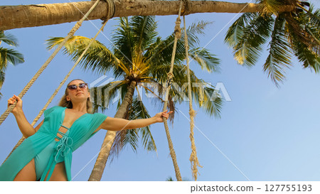 Seductive woman swinging on a swing on a tropical beach, on shores of the turquoise sea. Concept travel, walks, rest in sea, tropical resort coastline relaxation traveling tourism summer holidays. 127755193