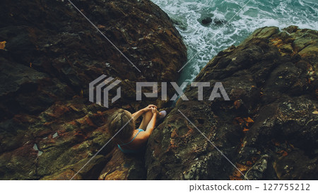 Woman meditates, relaxes on rock crack reef hill in stormy morning cloudy sea. Concept feminine, sexual vaginal health, womanly, freedom, freshness 127755212