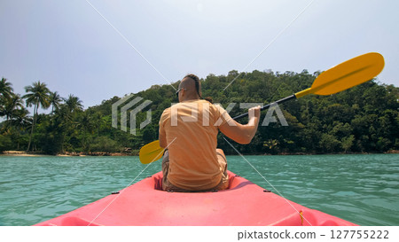 Man with sunglasses and hat rows pink plastic canoe along sea ag Man with sunglasses and hat rows pink plastic canoe along sea ag 127755222